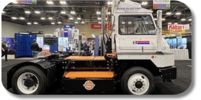 A side view of an electric truck displayed at an exhibition, showcasing a white cab with the text 'PURE ELECTRIC' and orange accents on the chassis.